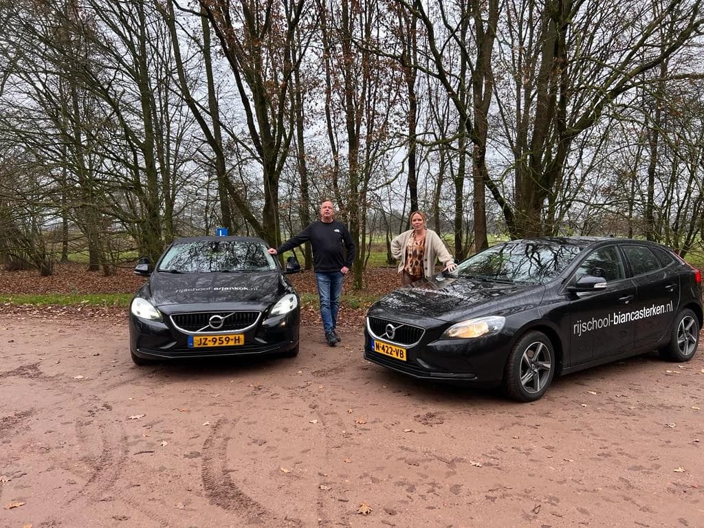 Instructeurs Arjan Kok en Bianca Sterken leunend tegen hun lesauto's in het bos.